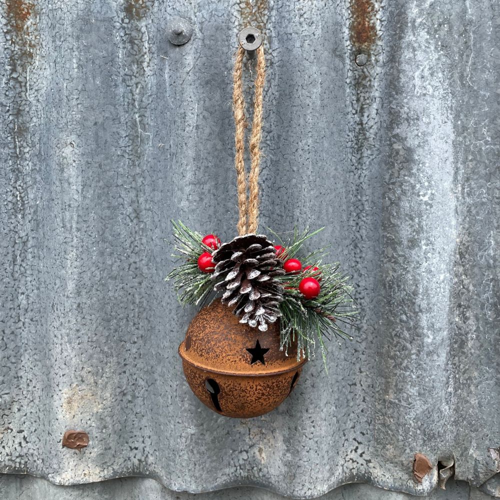 Decorative rusty bell with pine cone and berries hanging against a corrugated metal background