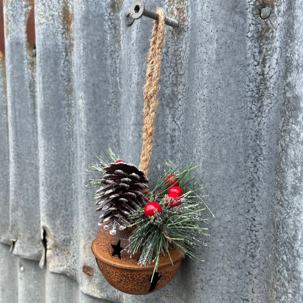 Decorative rusty bell with pine cone, red berries, and greenery on a metal surface.