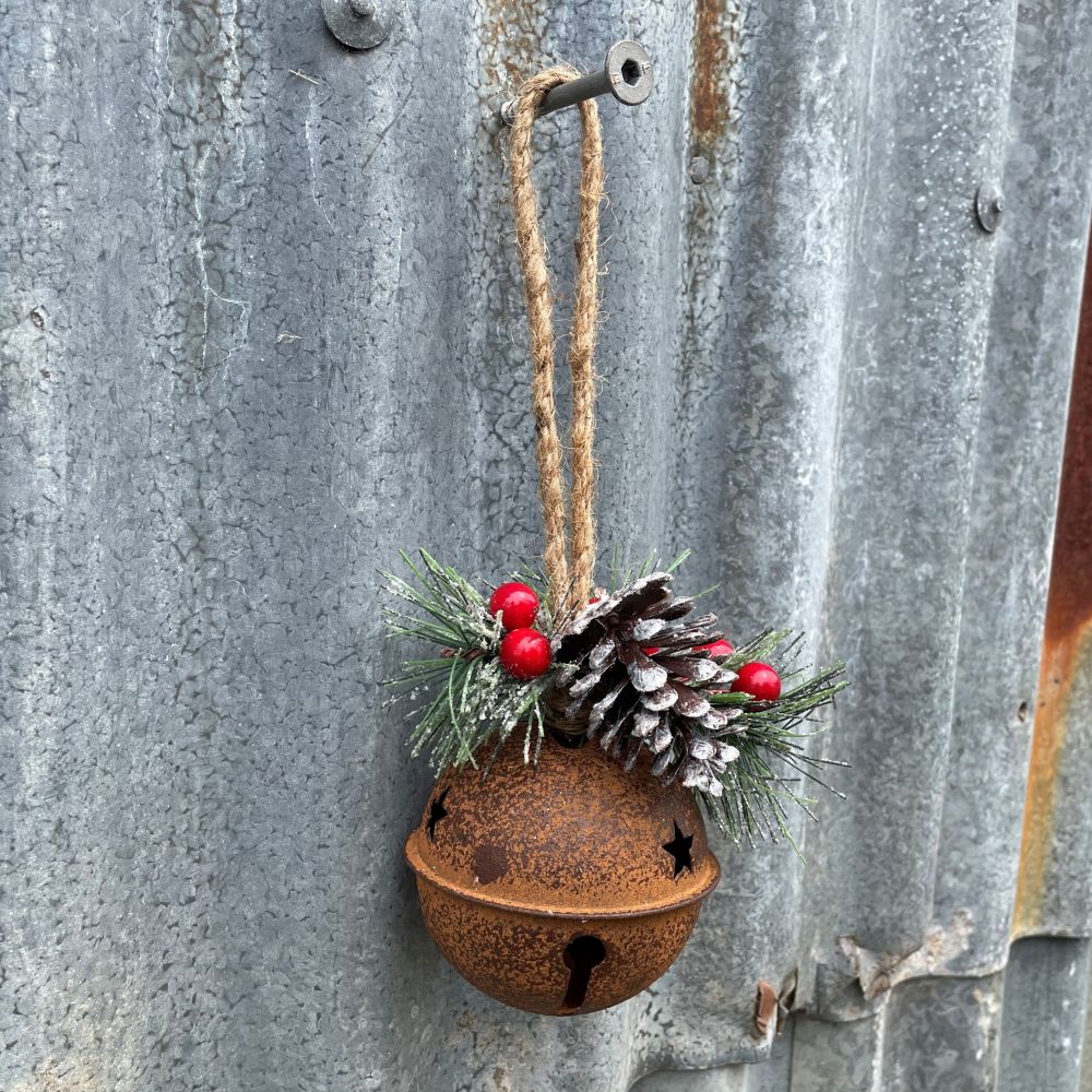 Decorative rusty bell with pine cones and berries hanging on a metal surface