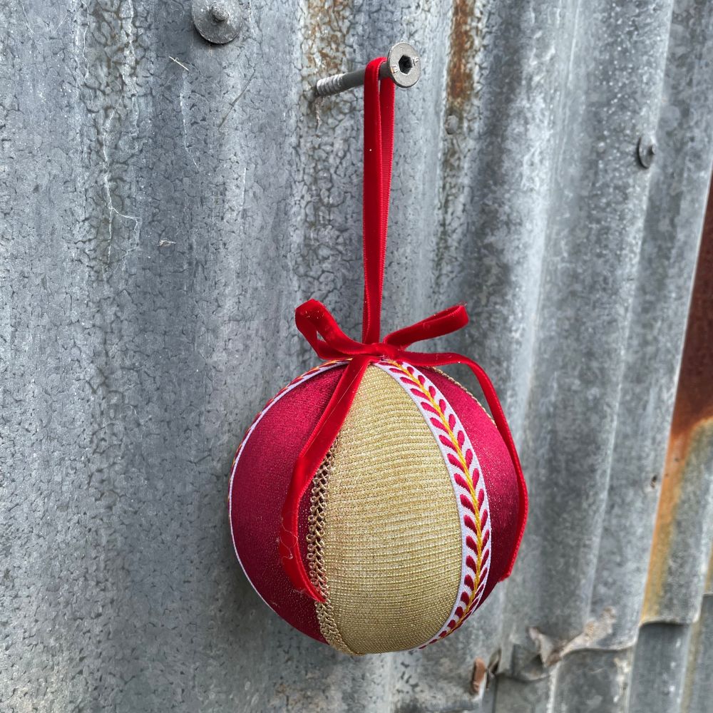 Velvet round bauble in red and gold fabric with gold and patterned braiding and red velvet bow on corrugated iron wall