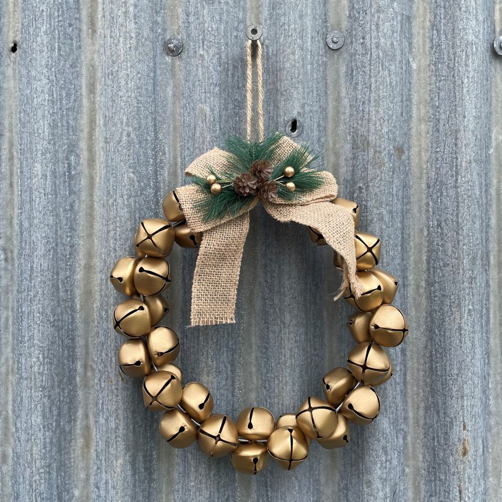 Wreath made of gold bells with a jute bow and greenery on a rustic metal background