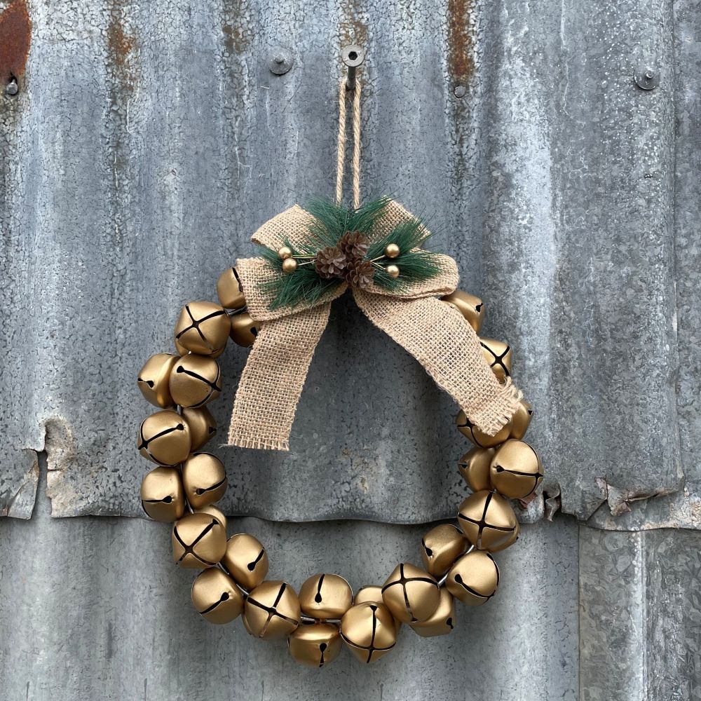 Decorative wreath with gold bells and a jute bow on a rustic metal background