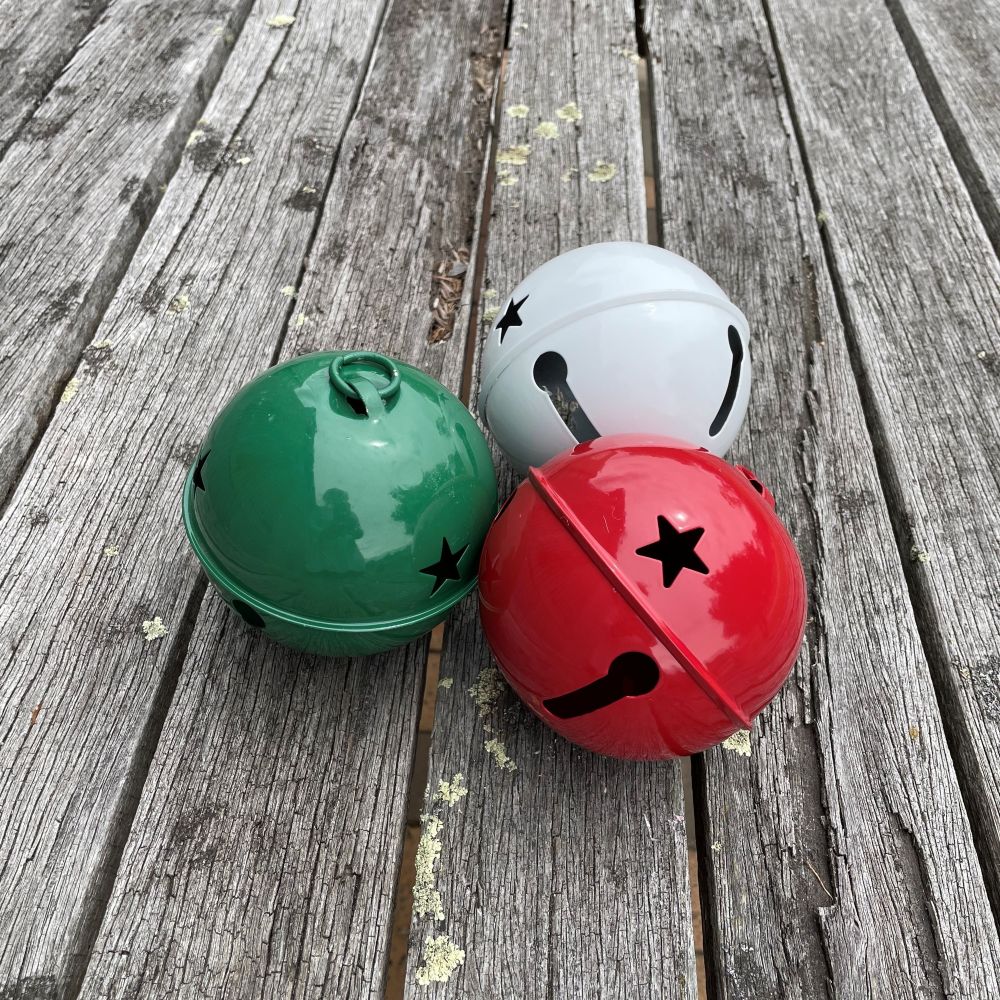 Three colorful jingle bells (green, white, red) on a wooden surface.