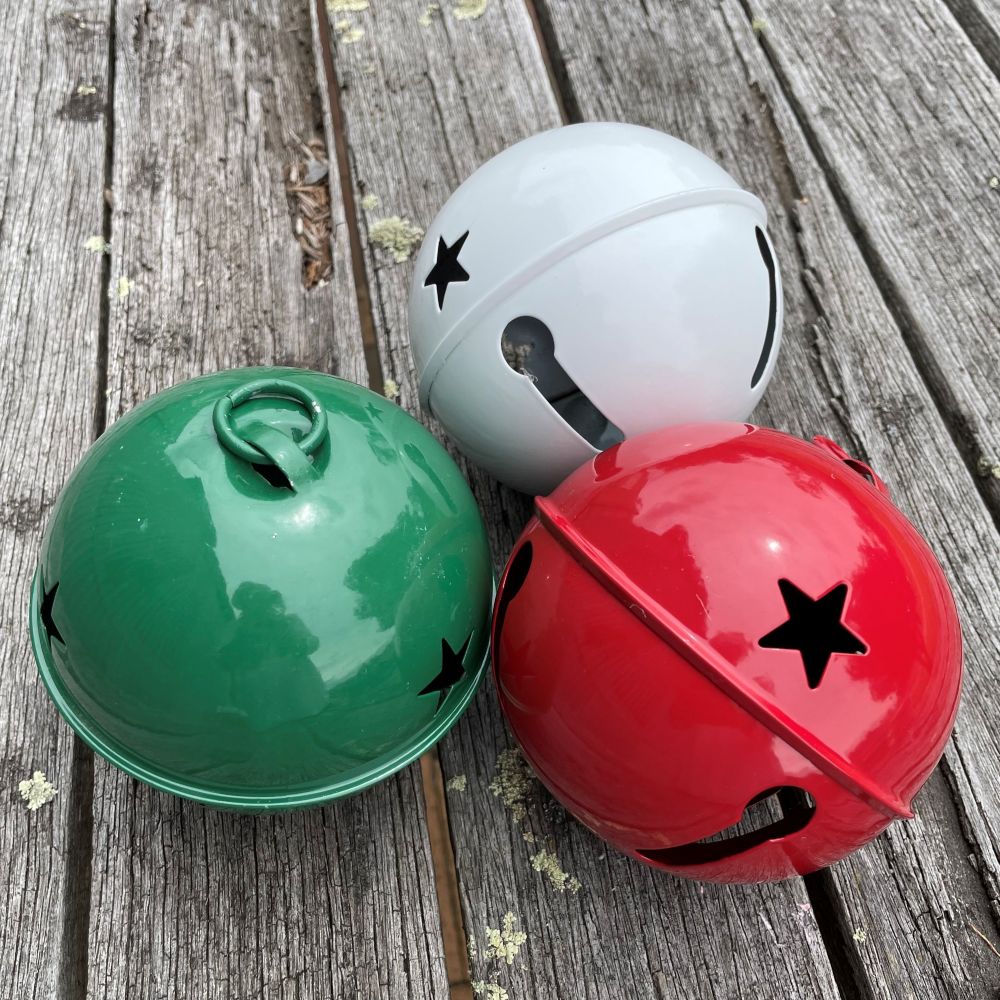 Three colorful jingle bells (green, white, red) with star designs on a wooden surface.