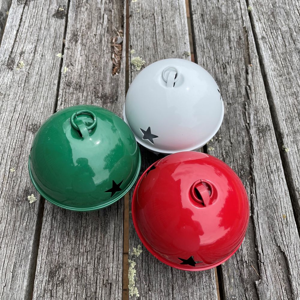 Three colorful bells (green, white, red) with star designs on a wooden surface -showing small hooks on top