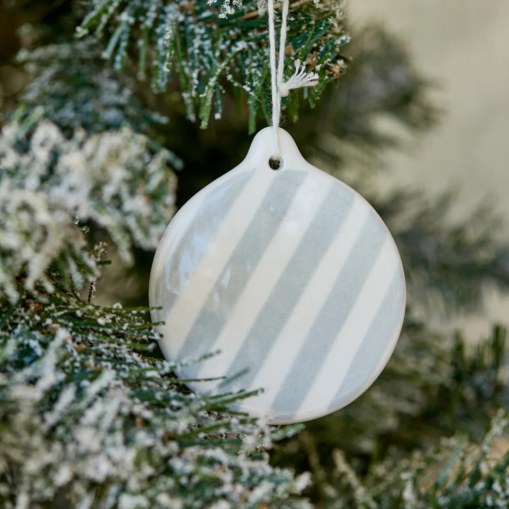 Round ceramic hand painted ornament with light blue and white stripes hanging on a Christmas tree