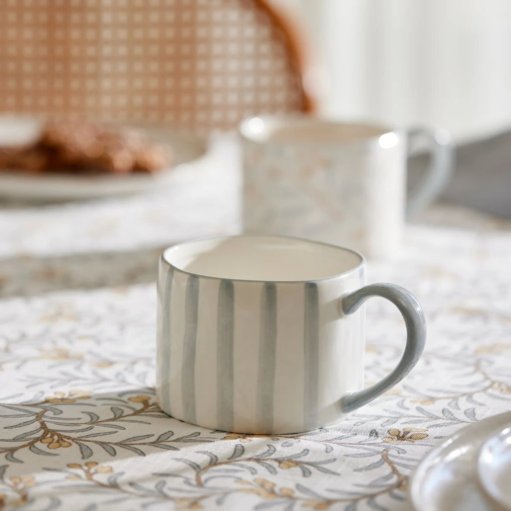Blue Striped ceramic mug on a juniper -patterned tablecloth with a blurred background
