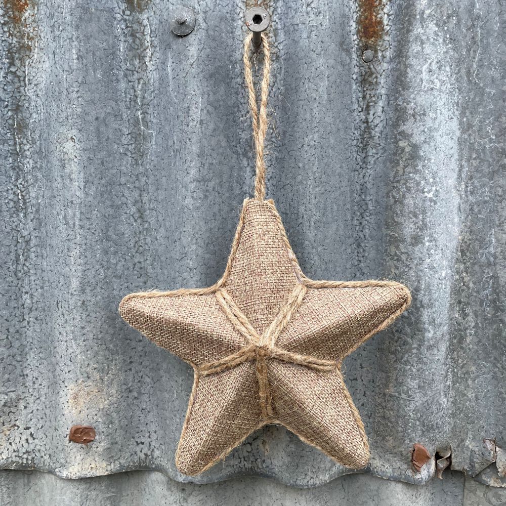 Star ornament made of linen-look fabric and jute detailing hanging on corrugated iron background