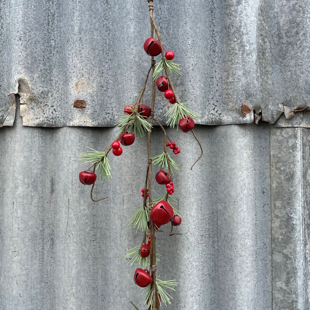 Decorative garland with red bells and greenery hanging against a corrugated metal background