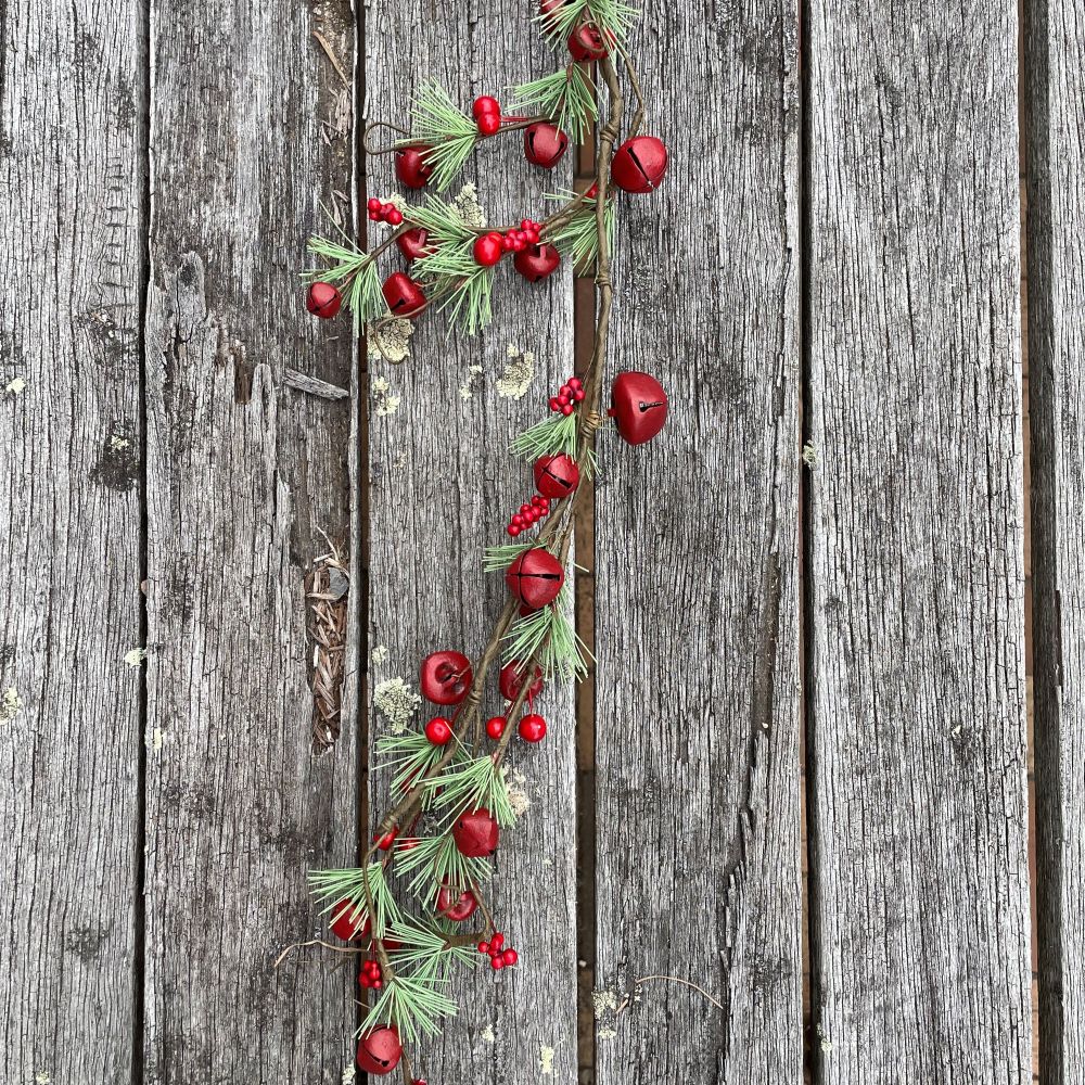 Decorative garland with red berries, red bells and pine needles on a wooden background