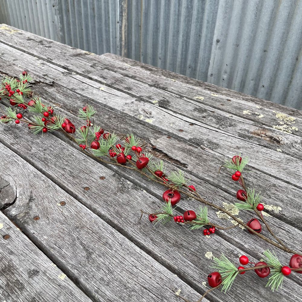 Decorative garland with red berries, red bells and pine needles on a wooden background