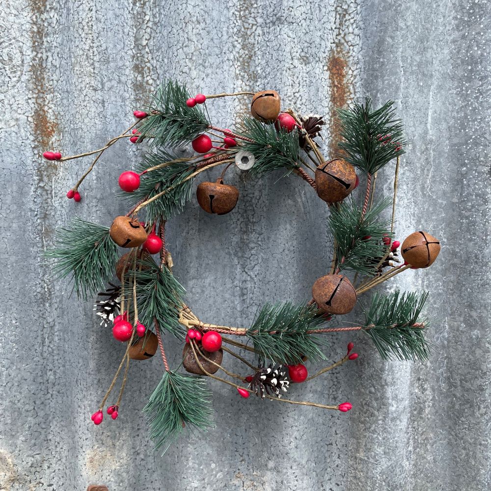 Christmas candle wreath with pine cones, red berries, and bells on a textured metal background