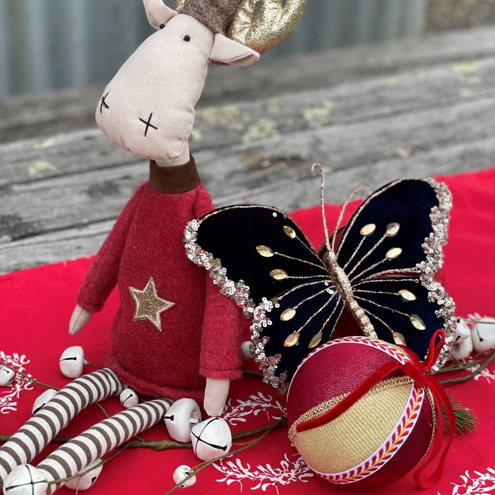 Carnival Christmas centrepiece with red table runner and display of moose, butterfly and velvet bauble decorations.