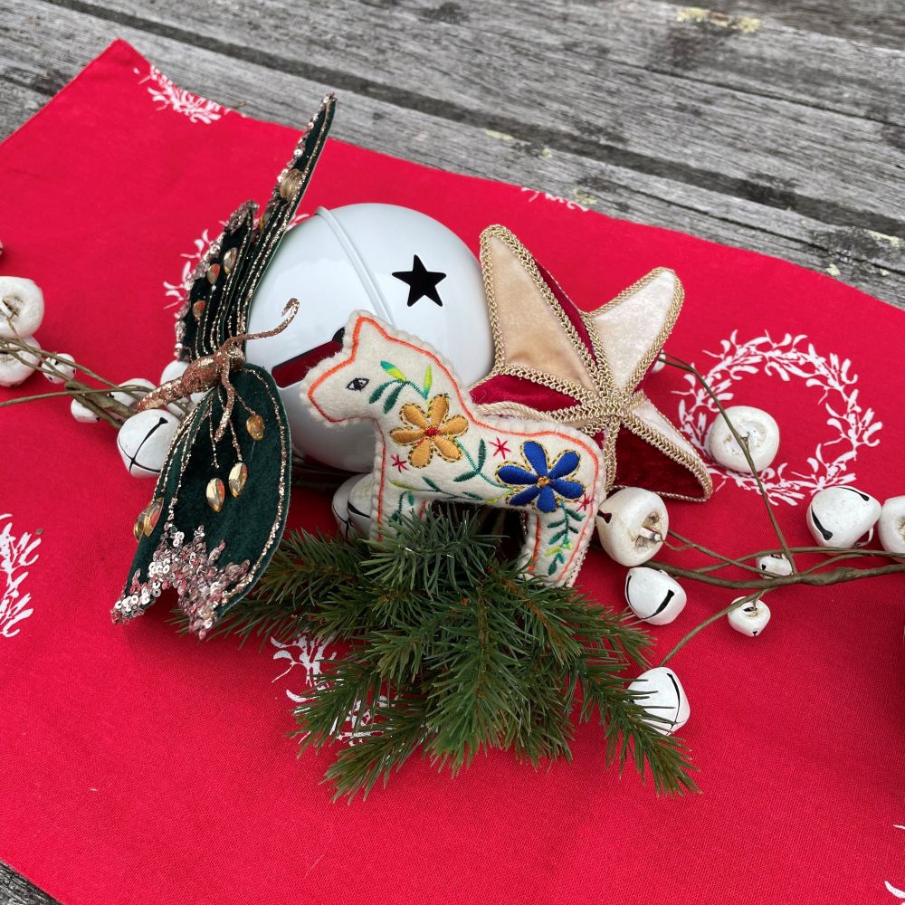 Carnival Christmas table centrepiece with red table runner and a display of velvet red and gold star, embroidered horse, white bells, and blue butterfly
