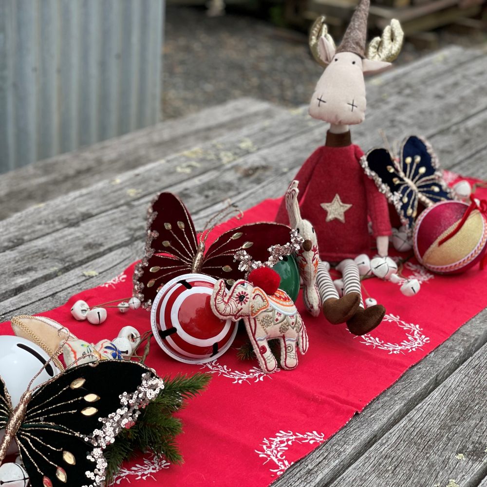 Decorative items displayed as a Christmas centrepiece including a plush reindeer, butterfly, and elephant on a red cloth with a wooden surface background.