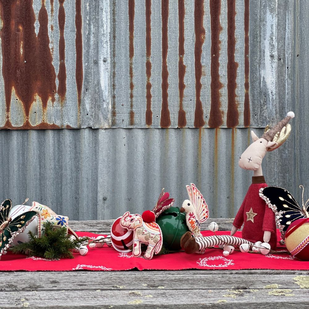 Decorative items displayed as a Christmas centrepiece including a plush reindeer, butterfly, and elephant on a red cloth with a wooden surface and corrugated iron wall behind.