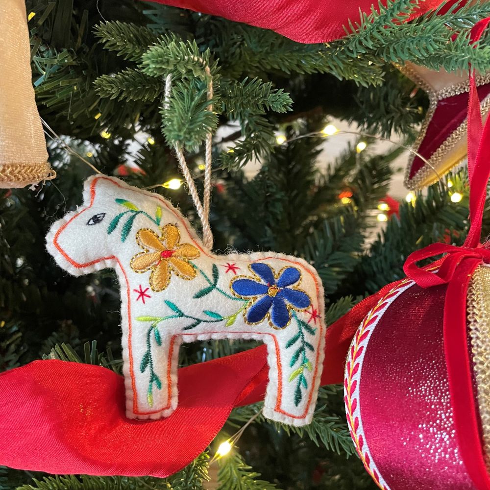 Decorative felt horse ornament with floral patterns hanging on a Christmas tree.