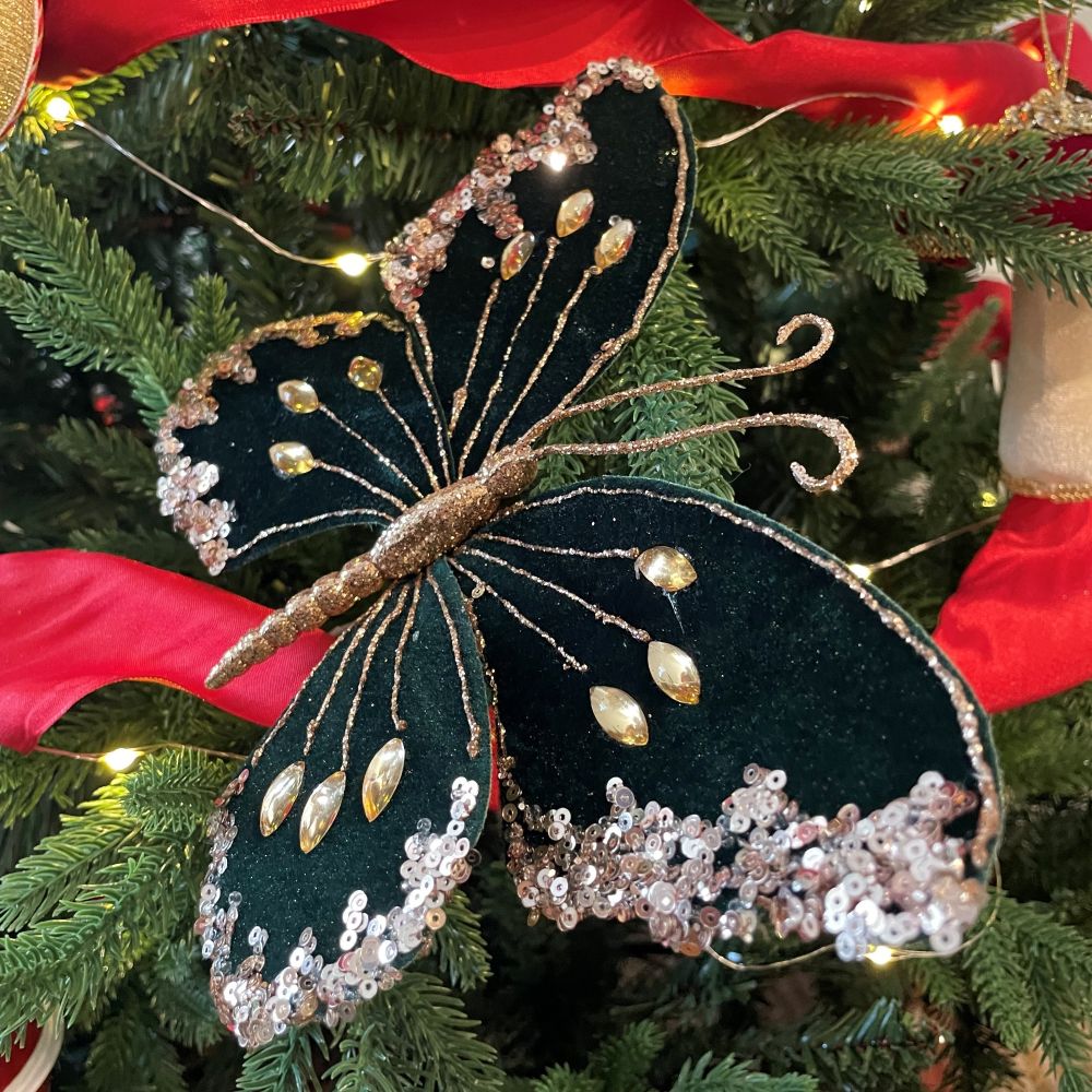 Decorative dark green butterfly ornament on a Christmas tree with red ribbon and lights.