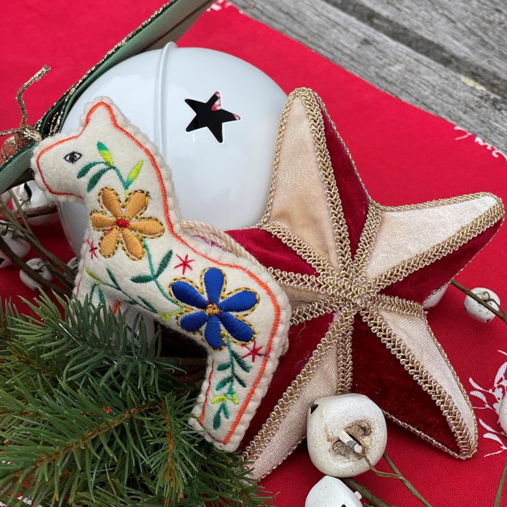 Carnival Christmas table centrepiece with red table runner and a display of velvet red and gold star, embroidered horse and white bells.