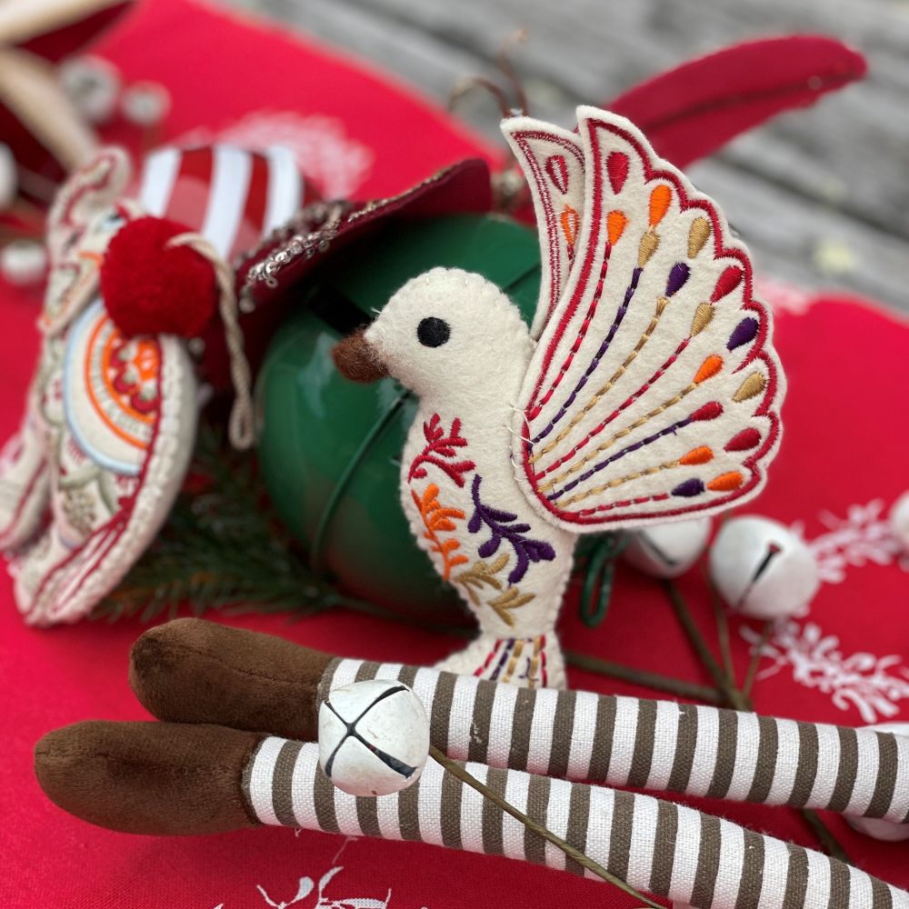 Decorative felt hummingbird ornament with colorful wings on a red background and other decorations around it