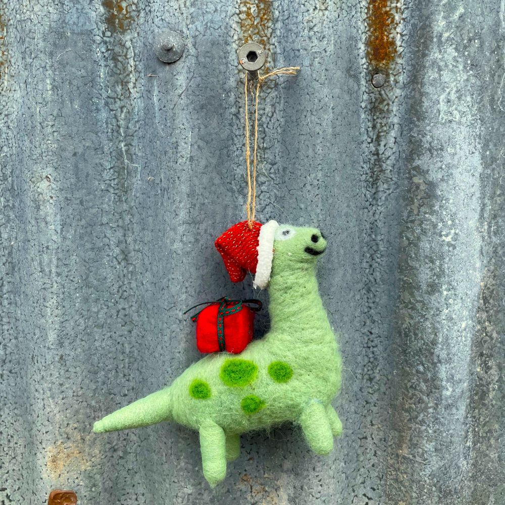 Green felt hanging dinosaur with a red gift on it's back and red santa hat  on a corrugated iron background