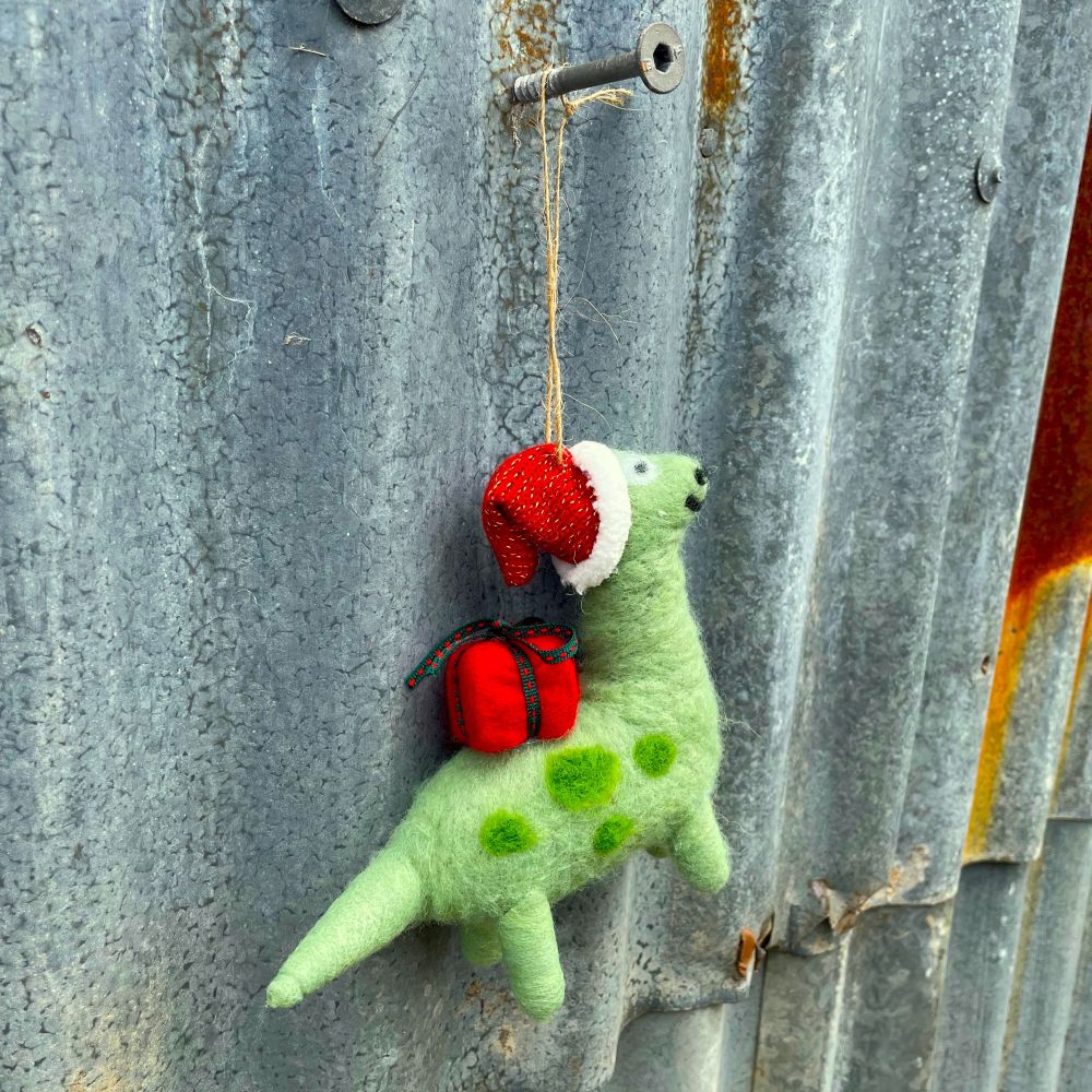 Green felt hanging dinosaur with a red gift on it's back and red santa hat  on a corrugated iron background