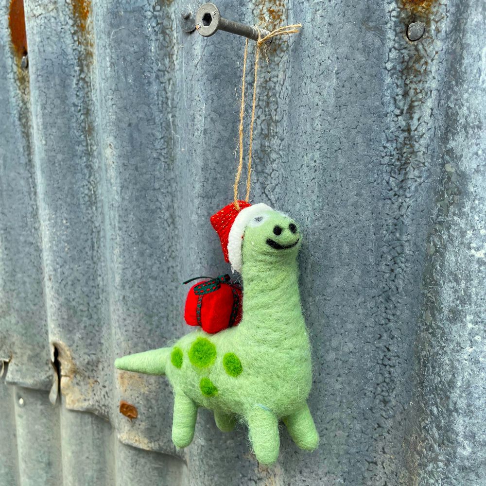Green felt hanging dinosaur with a red gift on it's back and red santa hat  on a corrugated iron background