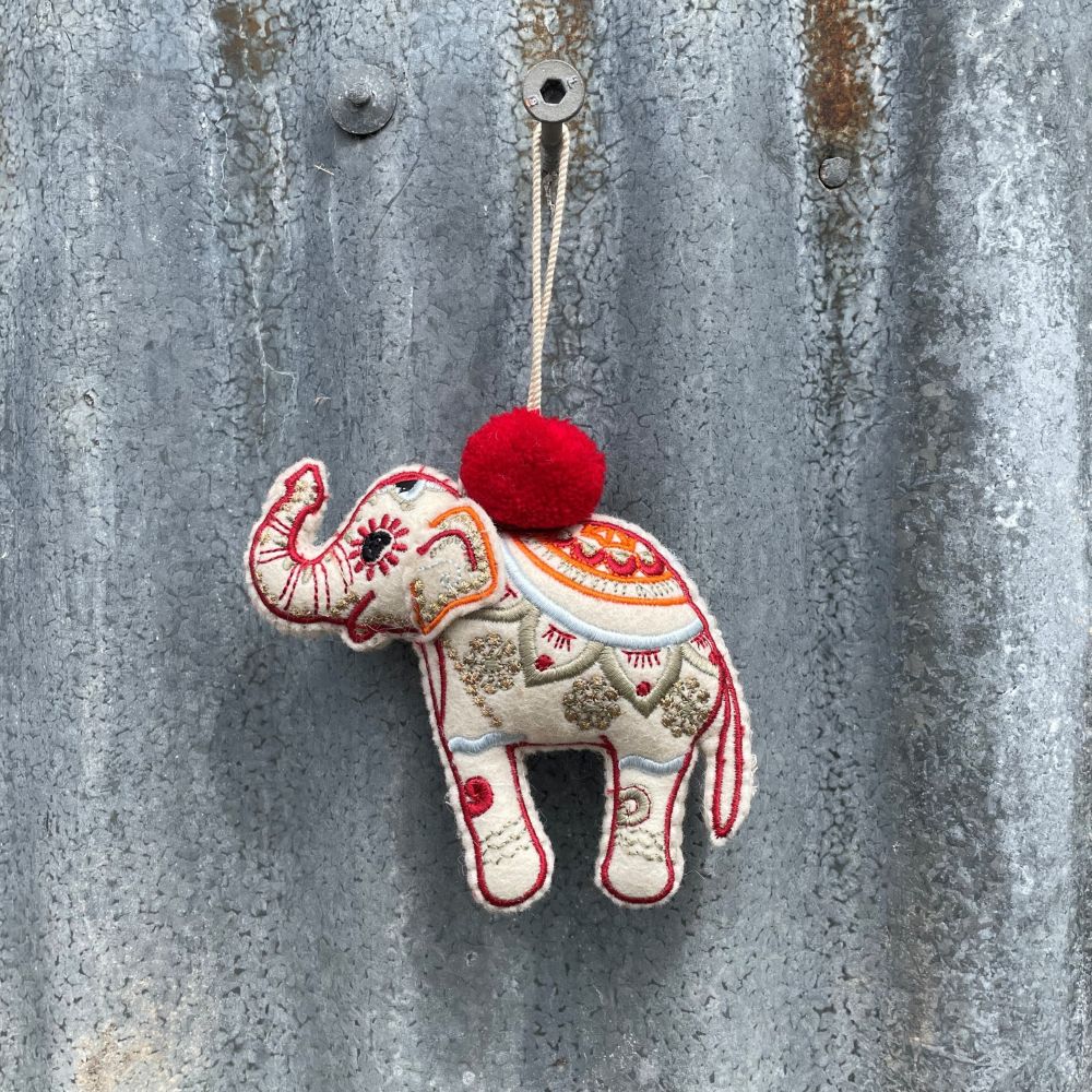 Decorative elephant ornament with a red pom-pom hanging on a textured metal surface.