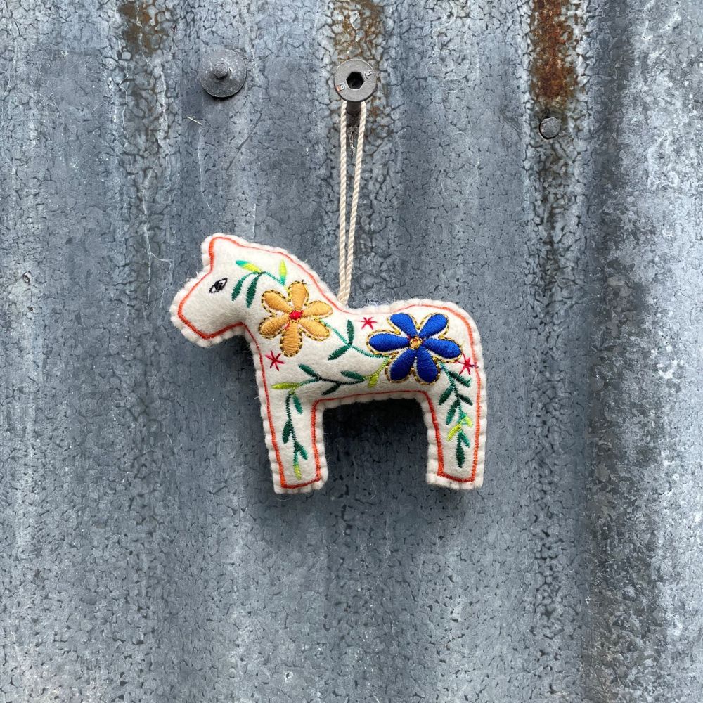 Decorative felt horse ornament with floral patterns hanging on a textured metal surface