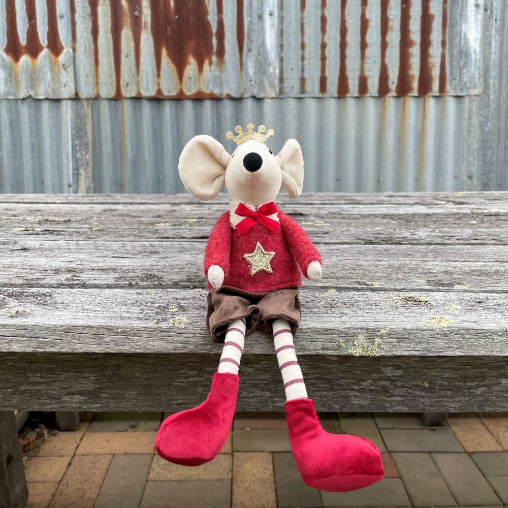 Fabric mouse decoration in a red outfit with a star and a crown on sitting on a wooden bench with legs hanging down