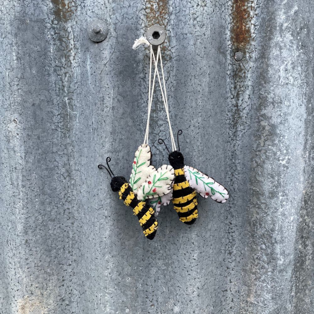 Two bee-shaped ornaments with black and yellow stripes on a rustic metal wall