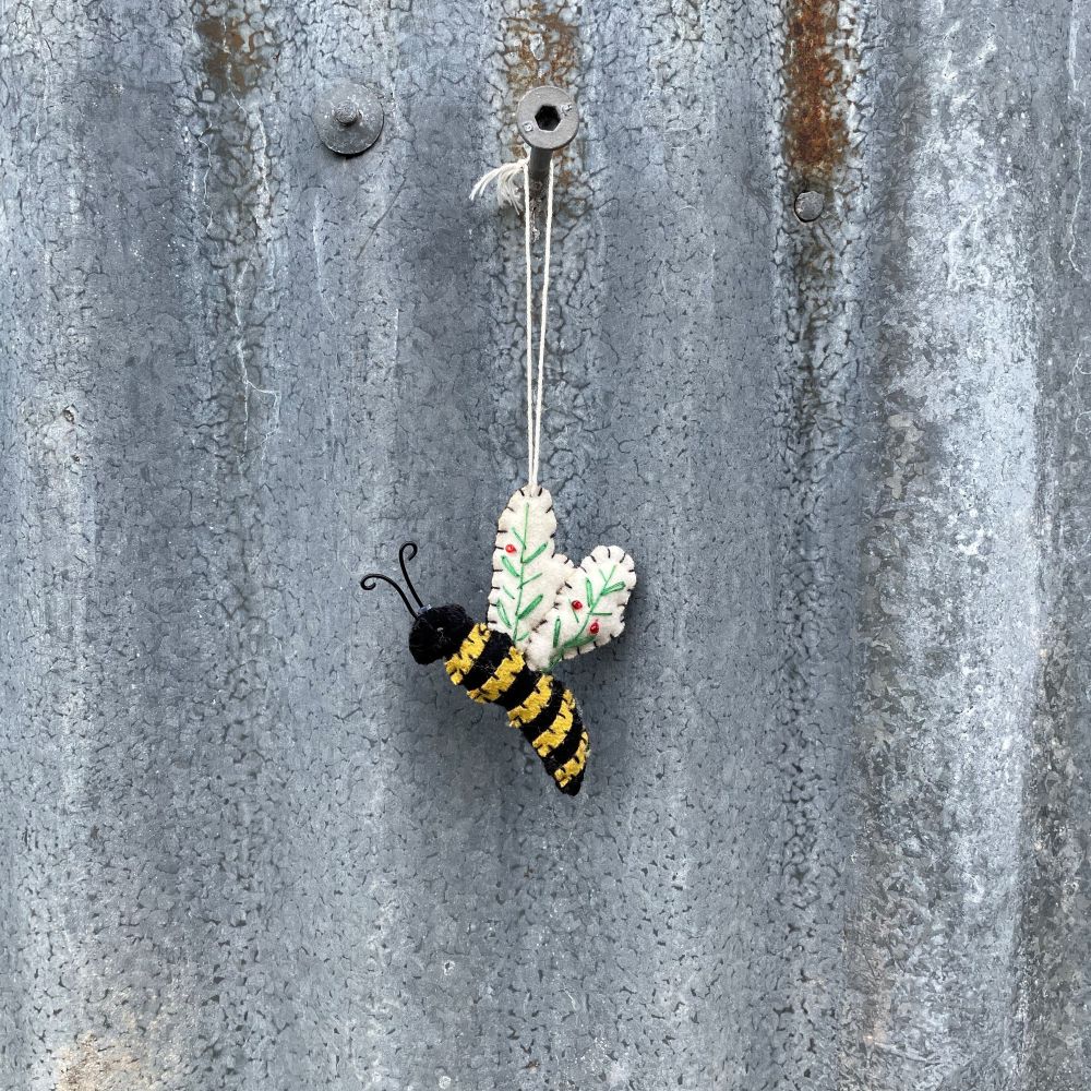 Decorative bee and flower ornament hanging on a textured metal surface