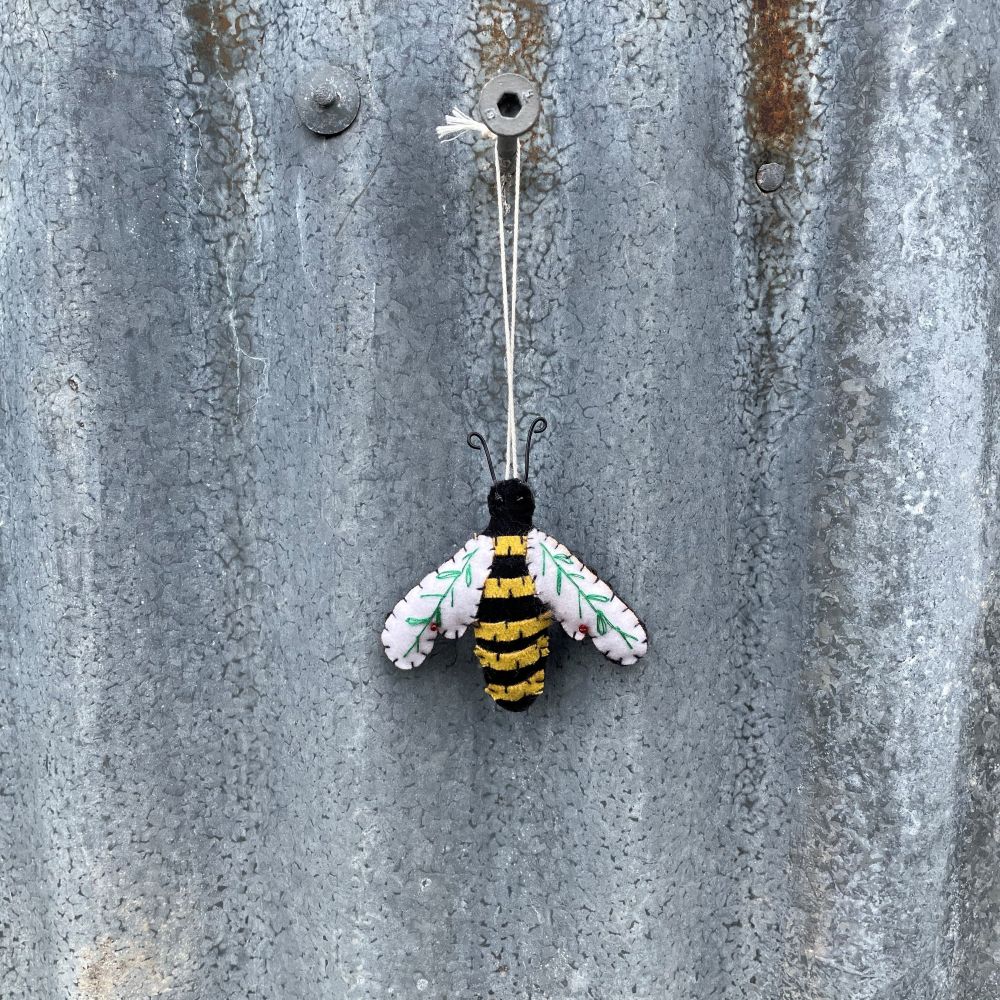 A bee-shaped ornament with black and yellow stripes on a rustic metal wall