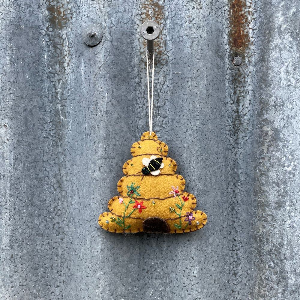 Decorative ornament shaped like a beehive with a bee and flowers on a rustic tin wall