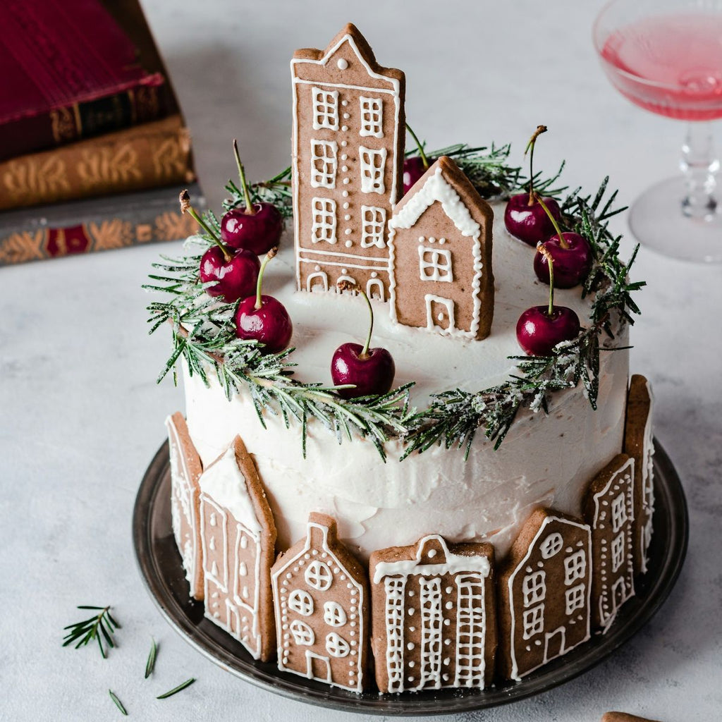 Decorative cake with gingerbread houses and cherries on a white surface