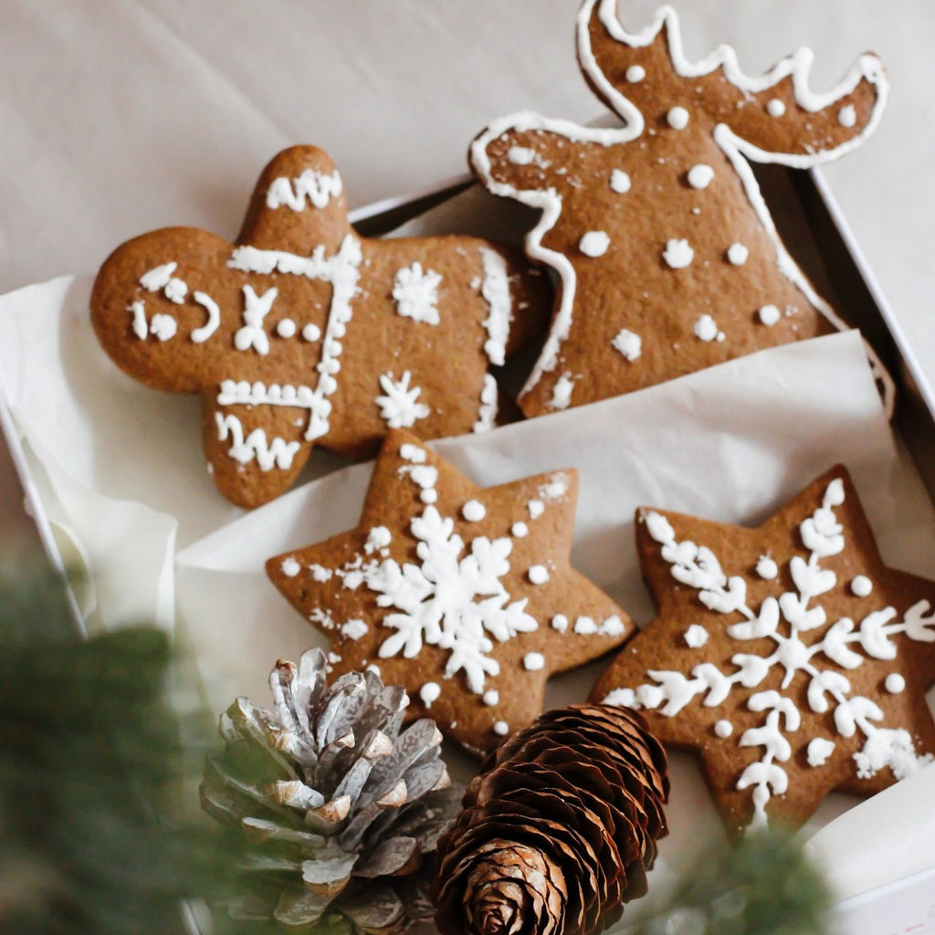 Decorative gingerbread cookies with white icing on a white surface with pine cones and greenery.