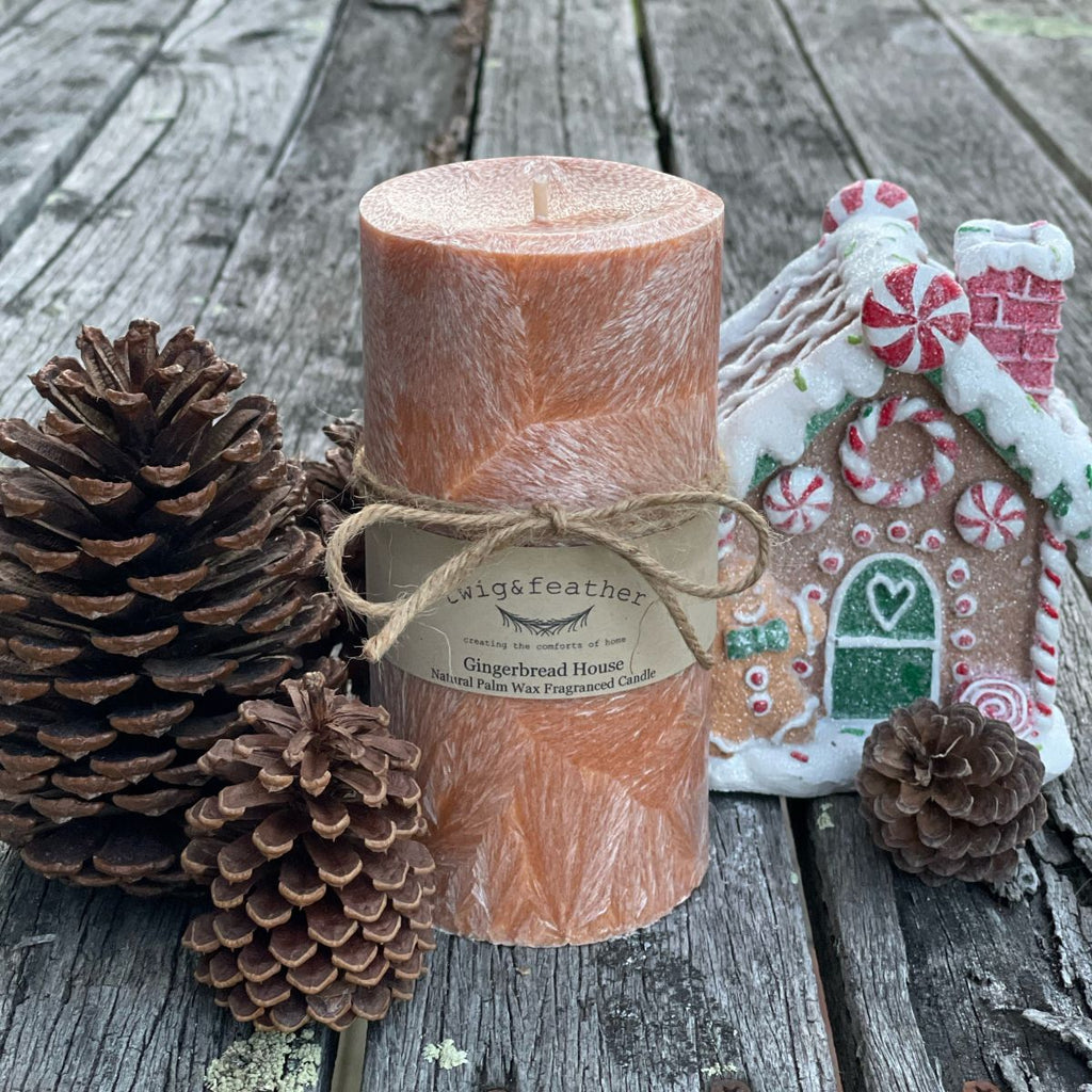 Twig and Feather Gingerbread house palm wax pillar candle (80 hours) with pinecones and a gingerbread house decoration on a wooden surface