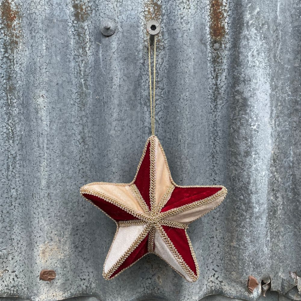 Velvet star decoration in red and gold with braiding hanging on corrugated metal background