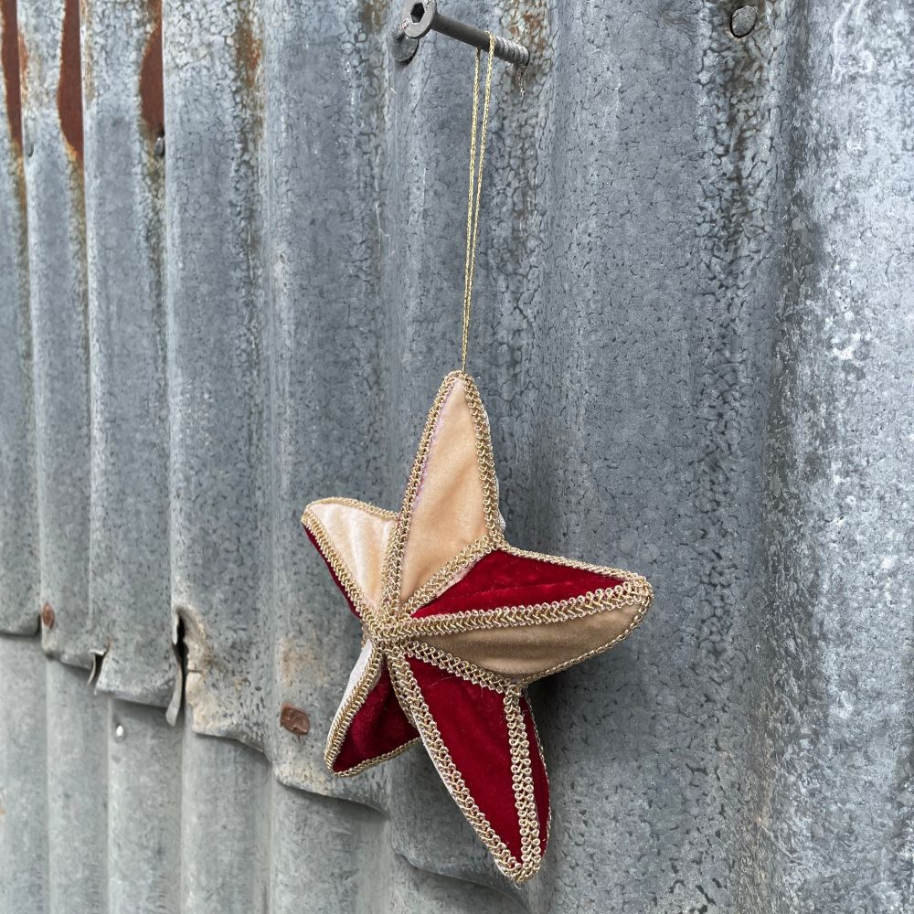 Velvet star decoration in red and gold with braiding hanging on corrugated metal background