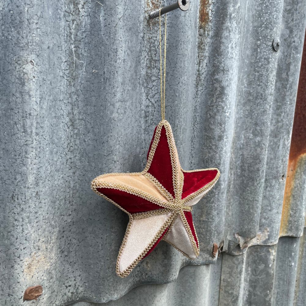 Velvet star decoration in red and gold with braiding hanging on corrugated metal background