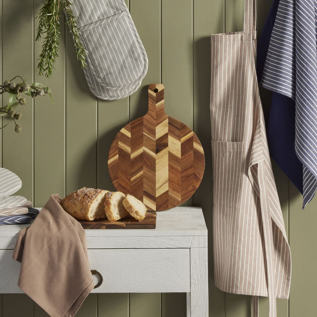 Wooden cutting board with bread on a white surface, apron, towel, and oven mitt in the background.