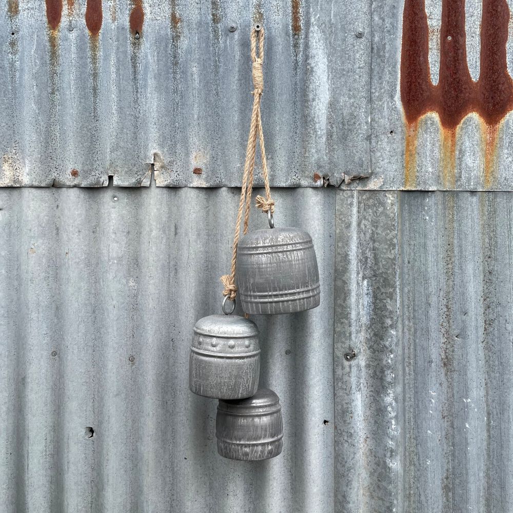 Three grey iron bells in different sizes hanging on a rusty corrugated metal wall