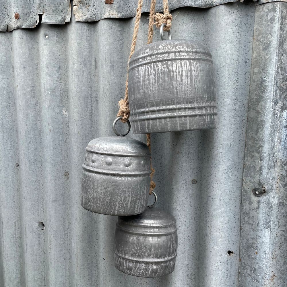 Three grey iron bells in different sizes hanging on a rusty corrugated metal wall - detailed view