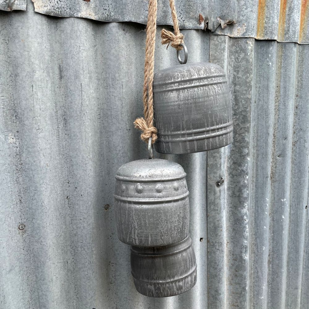 Three grey iron bells in different sizes hanging on a rusty corrugated metal wall - detailed view