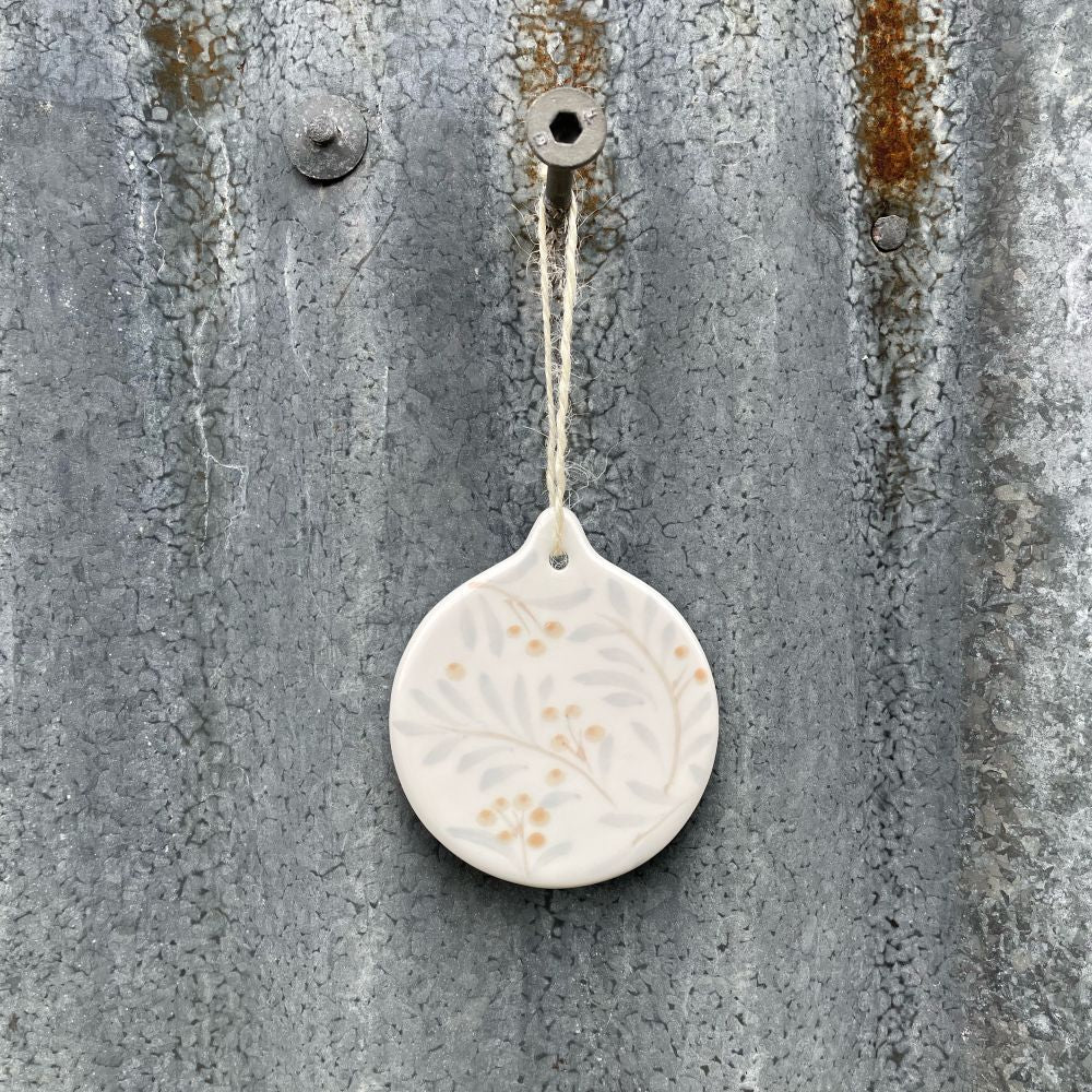 Round ceramic ornament with juniper pattern hanging on a textured metal surface