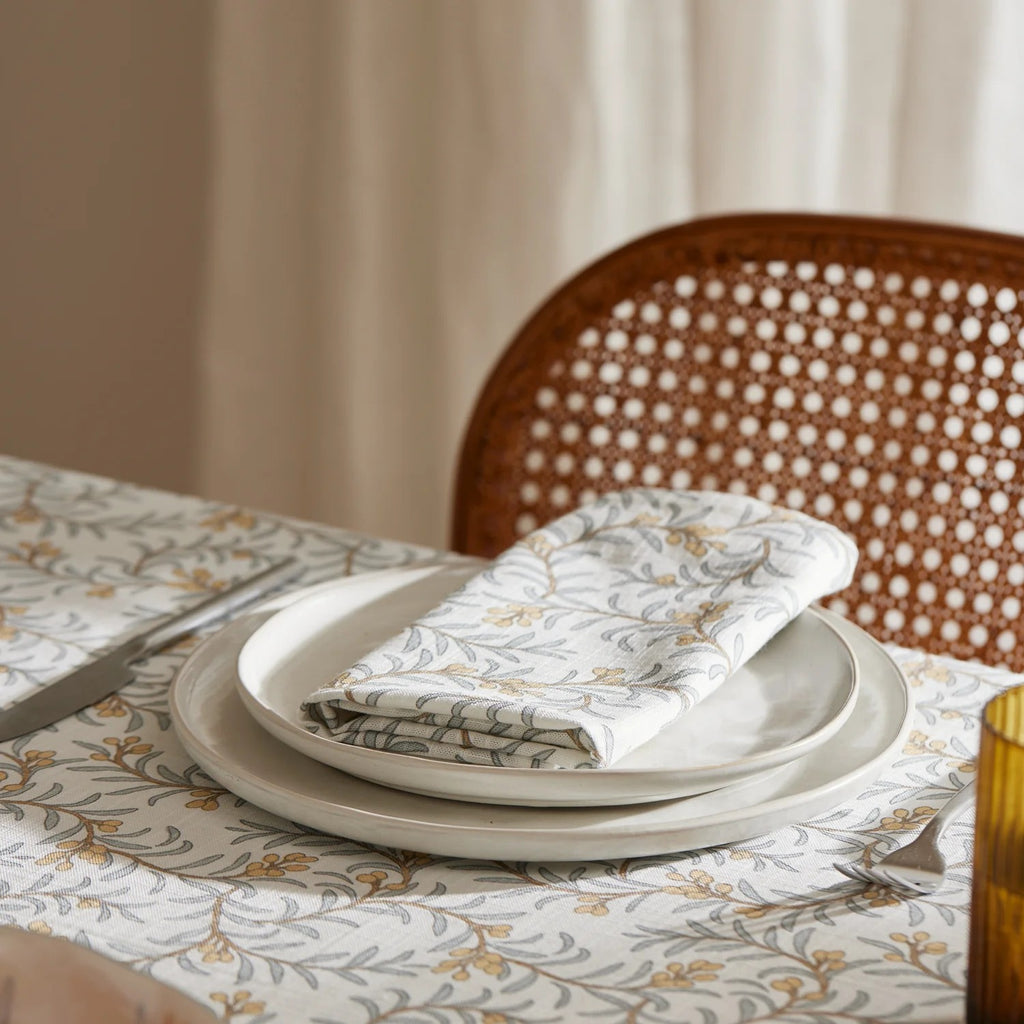 Juiper table setting on dining table with juniper napkin and plates on a patterned tablecloth depicting branches of blue leaves and apricot coloured berries.