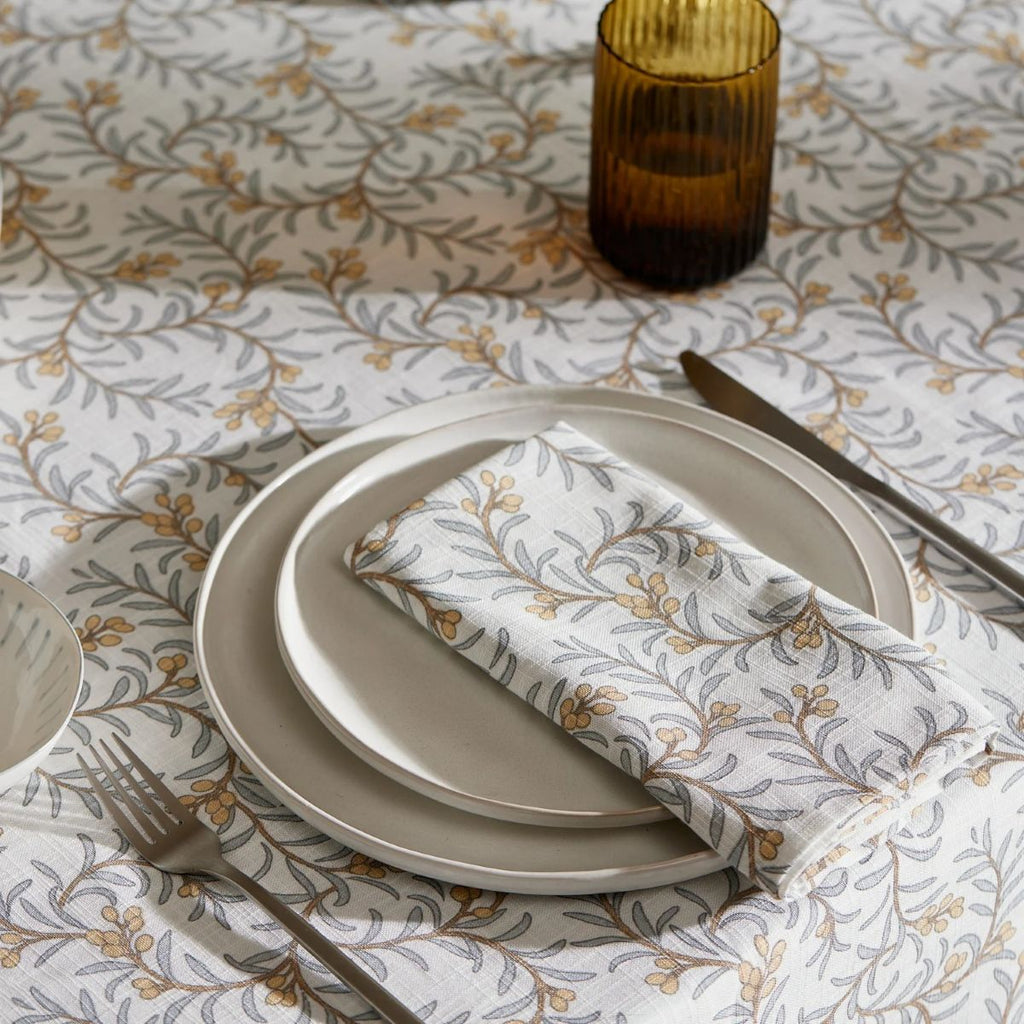 Juiper table setting on dining table with juniper napkin and plates on a patterned tablecloth depicting branches of blue leaves and apricot coloured berries.