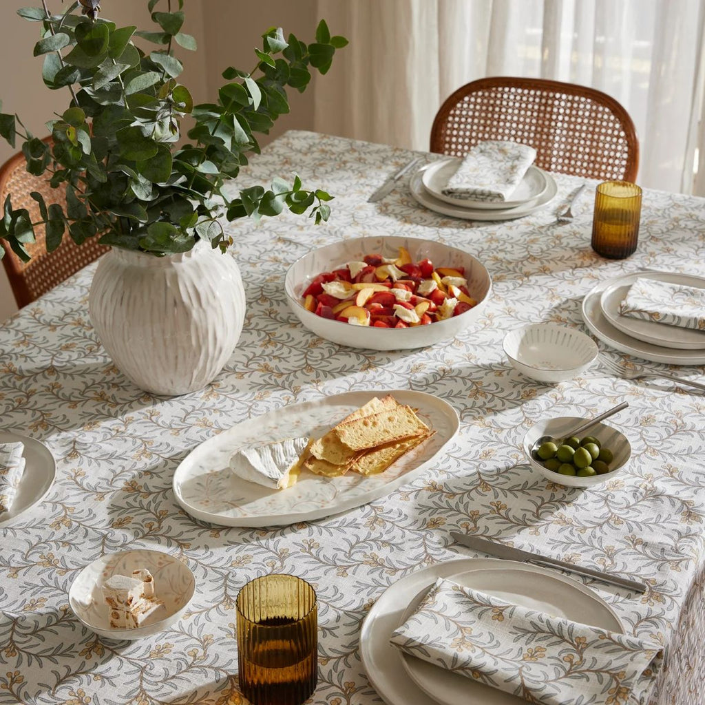 Dining table set with plates, bowls of food, and a vase with greenery using the Juniper napery of tablecloth and napkins in blue and apricot colours.
