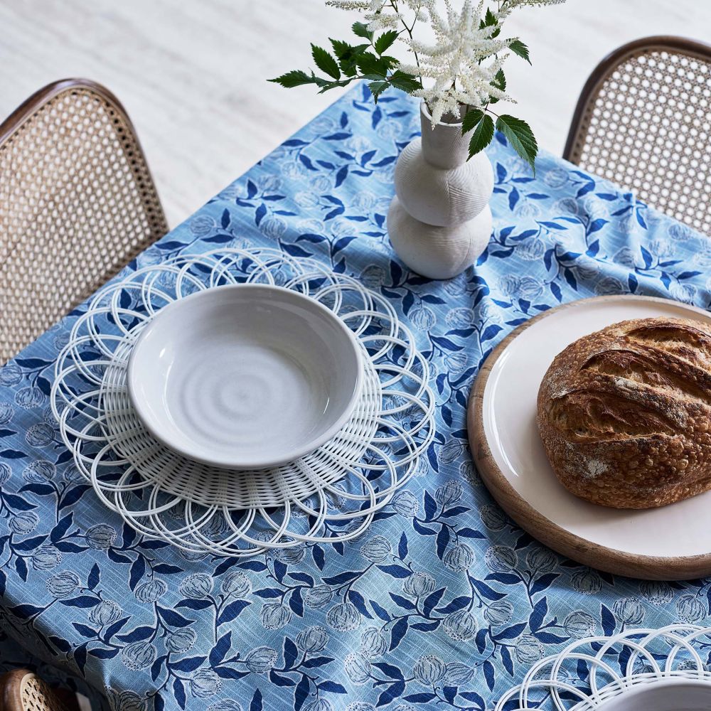 Table setting with a blue floral tablecloth, white plates, and bread.