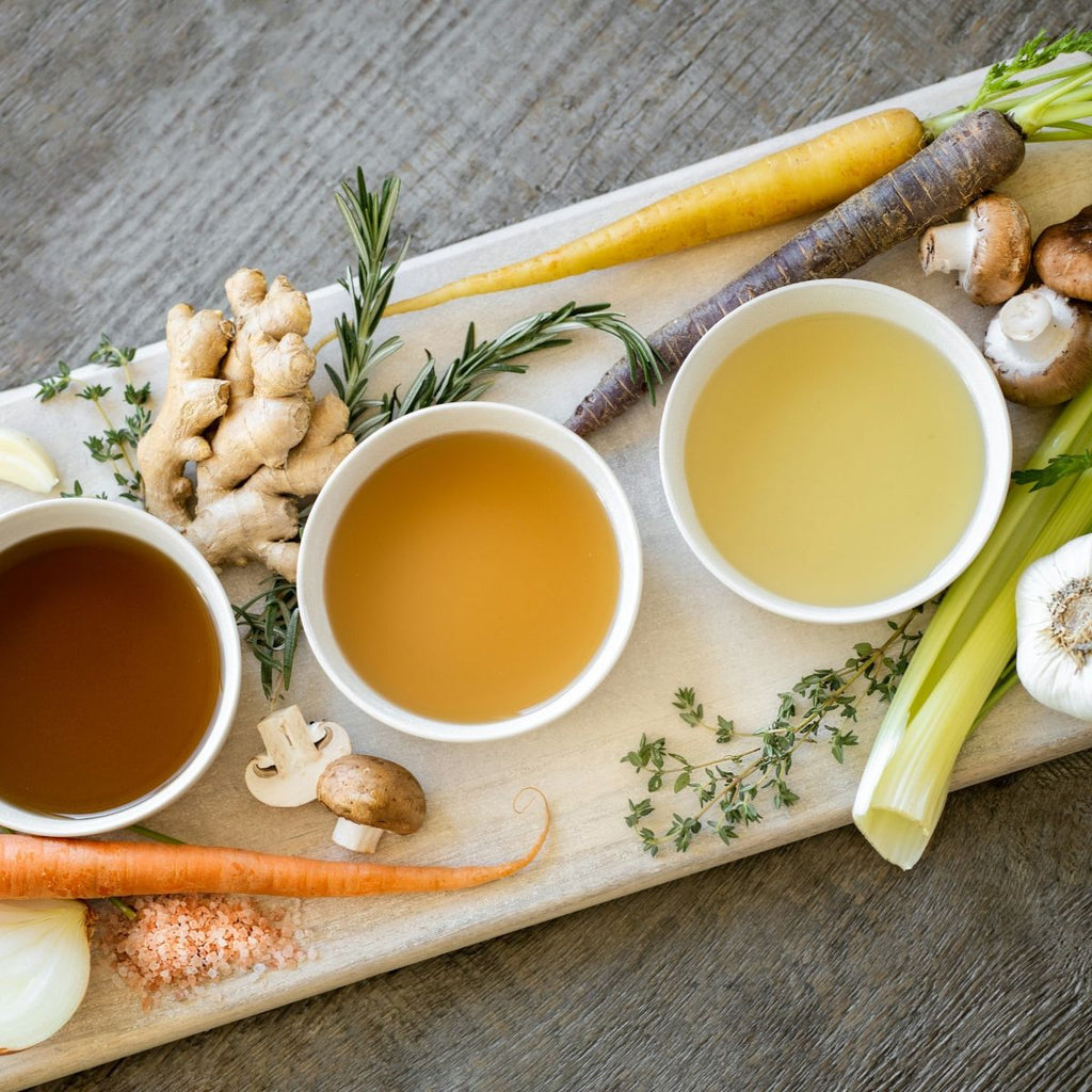 Three bowls of different teas on a wooden board with ginger and herbs.